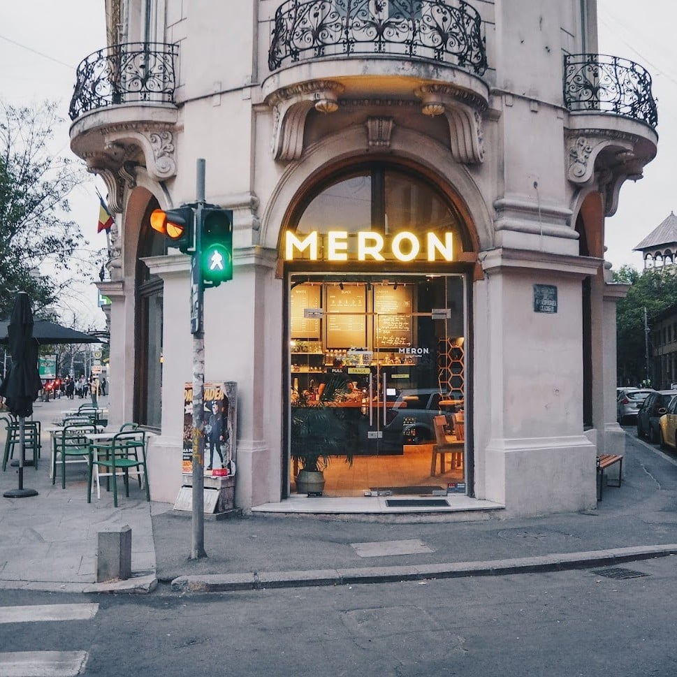 Meron se află într-o clădire istorică de colț, cu o intrare vizibilă și o terasă mică la stradă, ideală pentru pauze la cafea.