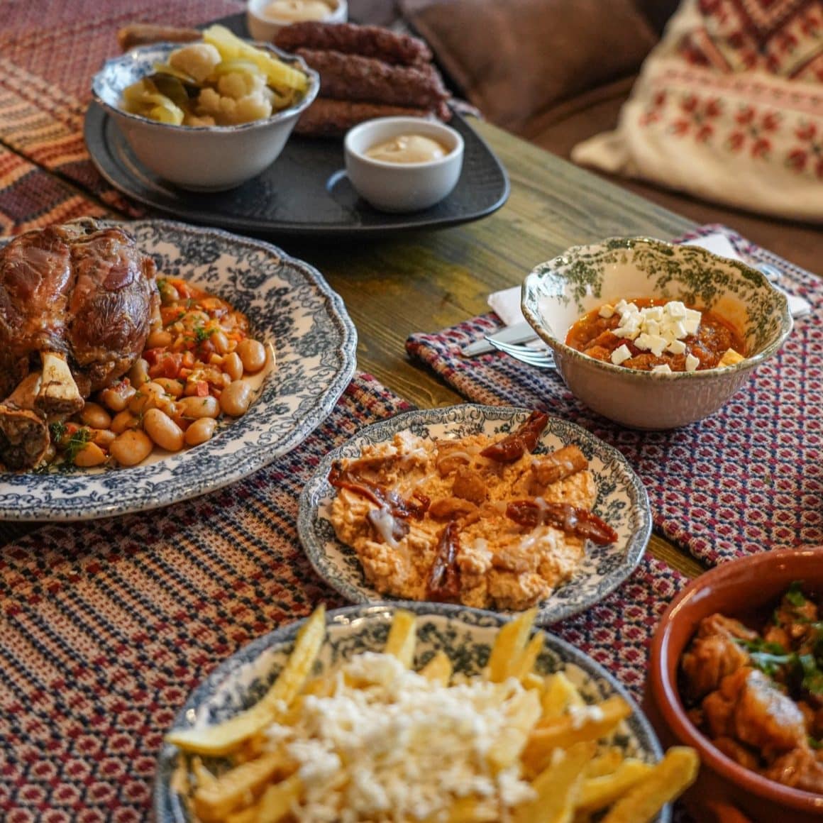 Mai multe farfurii de sharing cu tapas românești: salata de vinete, cartofi prajiti, iahnie cu ciolan, mici, murături