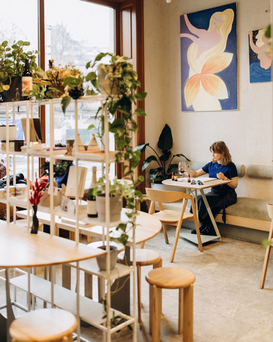 Femeie tanara la masa intr-o cafenea decorata cu tablouri si plante in ghiveci