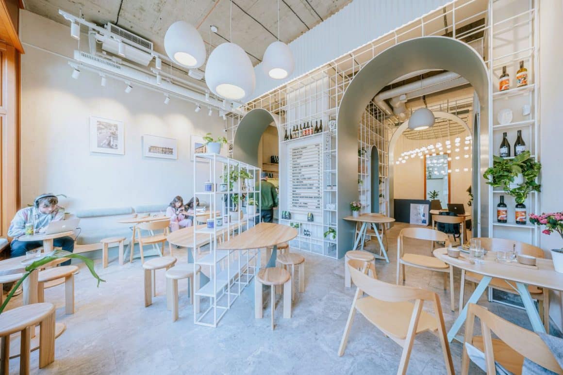 Interiorul Sip Coffee & Wine Bar, cu mult alb si mobilier din lemn natur, decorat cu sticle de vin, plante si lumini decorative