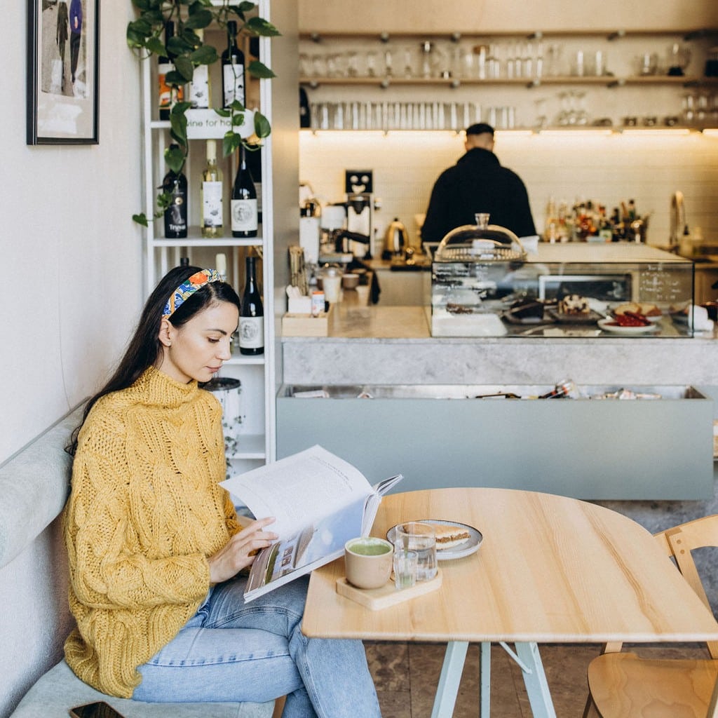 o tanara citeste o revista la masa intr-o cafenea.
