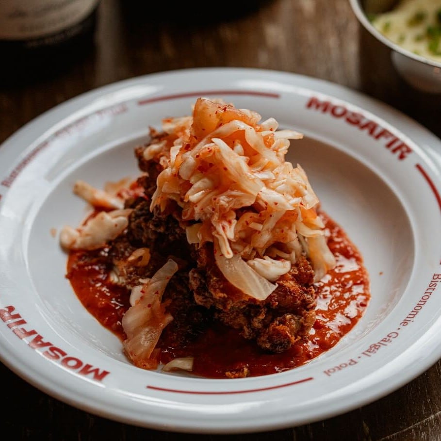 Pulpă de pui marinată în iaurt, boia dulce și usturoi, prăjită până la crustă crocantă și interior fraged. Se servește cu piure fin de cartofi, aromatizat cu dafin, varză proaspătă de la Obor, kimchi fermentat natural și un ketchup de casă - făcut din gogoșari și prune uscate.