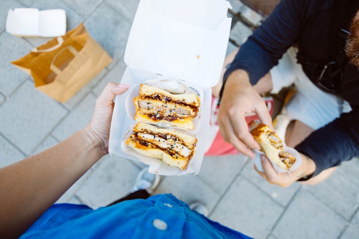 POV top down photo of woman hold delicious sandwich in take away box. Street food festival or food truck concept. Fast food with organic ingridients. Sharing concept. Sando, sandviș japonez