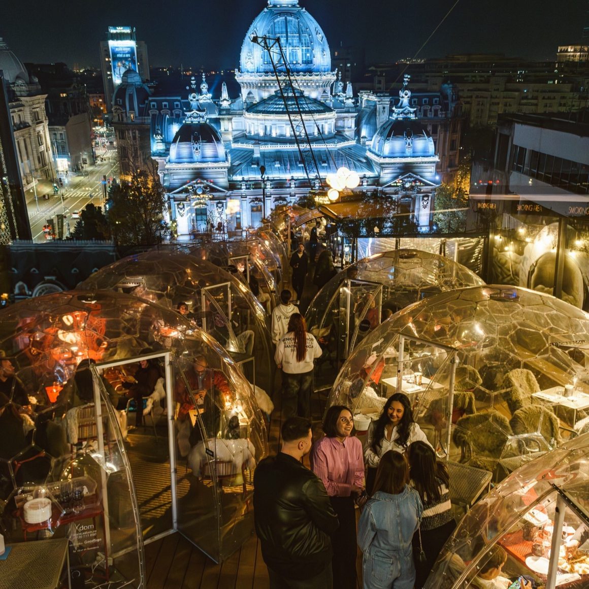igluurile de pe terasa Linea, fotografiate noaptea, cu o cladire luminata in fundal