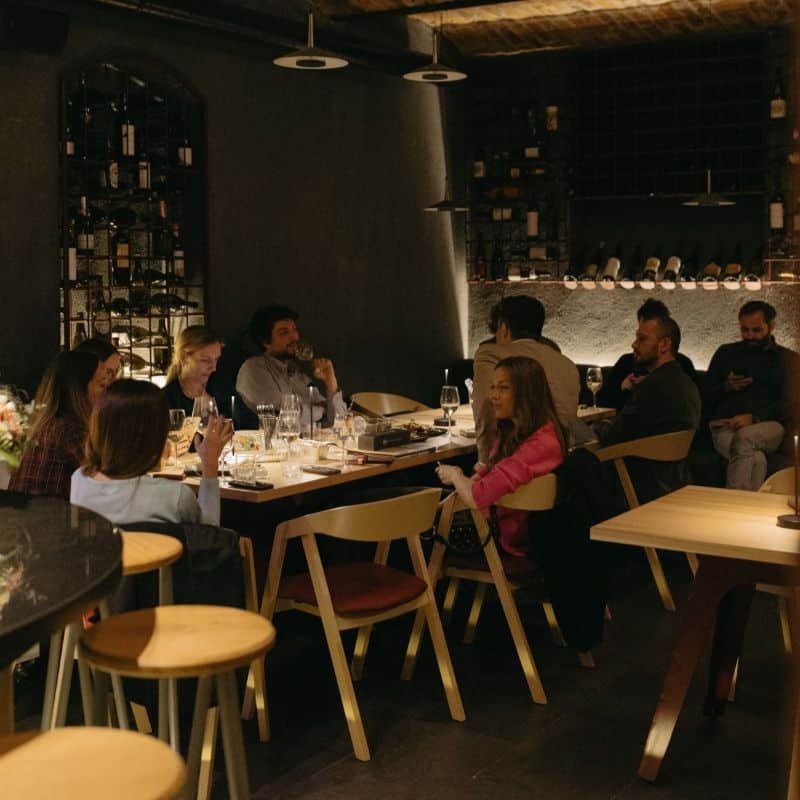 mai multe persoane asezata la masa in crama de la Sip Cofee & Wine bar, cu lumini difuze. Un loc potrivit pentru petrecerea de Crăciun a firmei