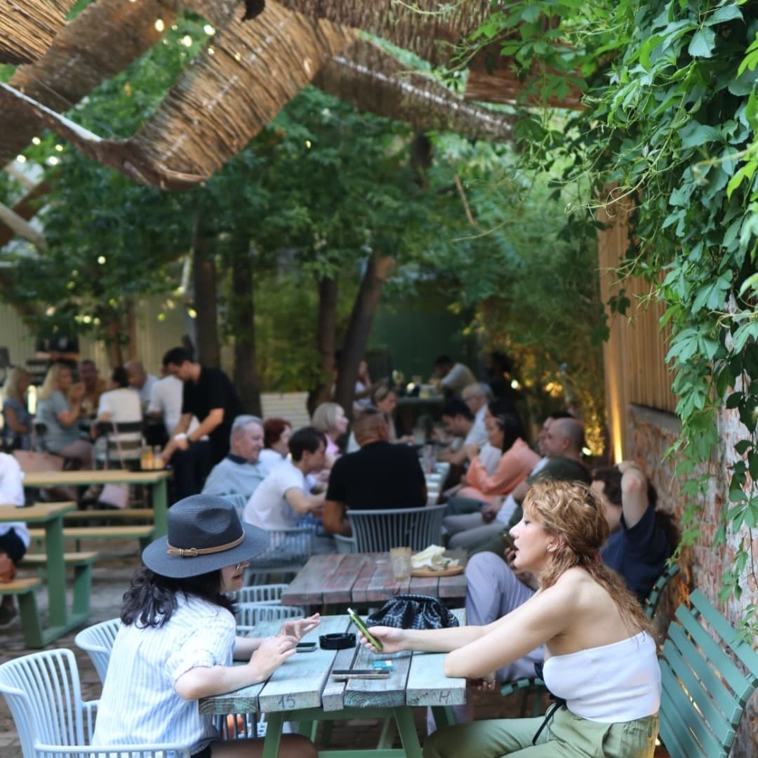 Terasa Bruma Coffee & Wine, cu mese din lemn printre verdeață, în plină zi