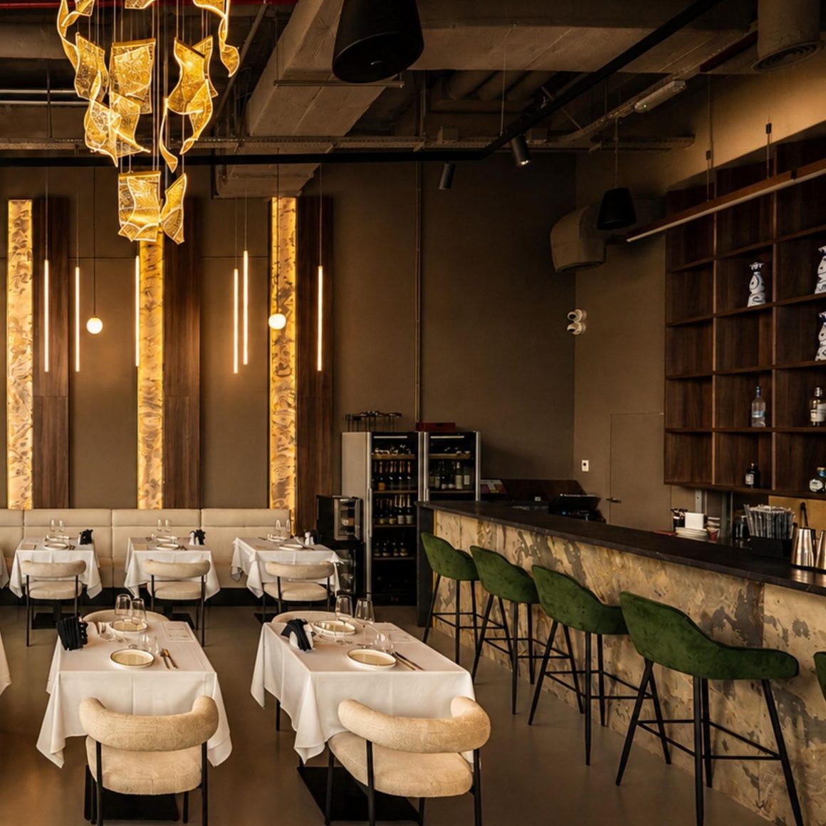 Barul Banco cu scaune înalte verzi și candelabru, văzut din sala restaurantului