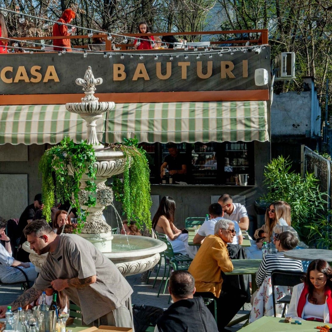 Mai mulți oameni stau la mese de vorbă, la Piațeta Cotroceni, o terasă cu vibe italian, unde bei un aperitivo bun în București