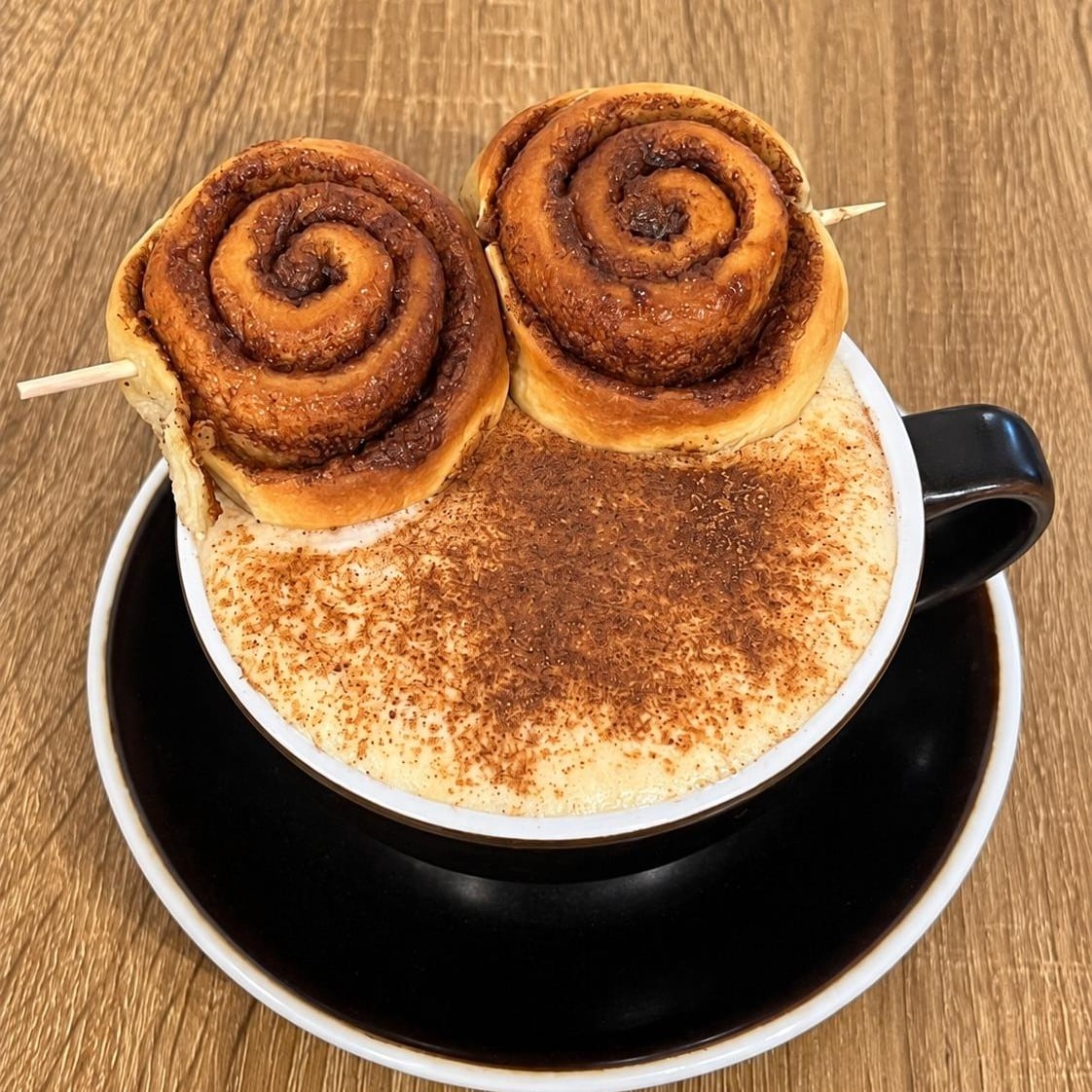 Cinnamon Roll Latte de la Cremma Café, cu spumă de lapte, scorțișoară și rulouri cu scorțișoară servite deasupra ceștii.