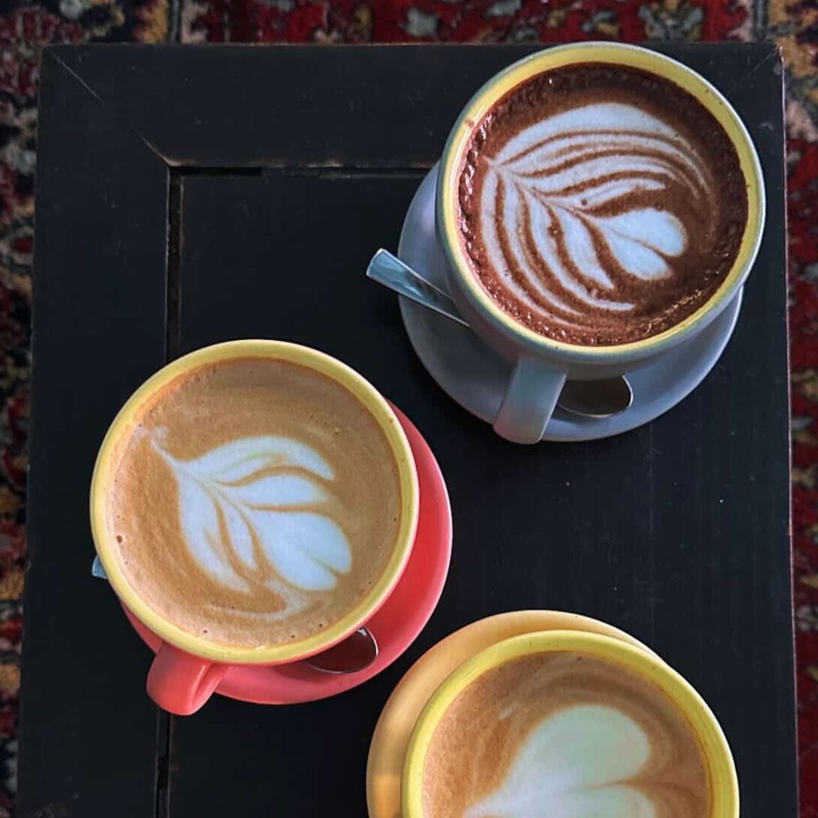 Latte-uri București la Twenty Eight Coffee, servite în cești colorate, cu latte art în modele delicate de frunze și spumă de lapte.